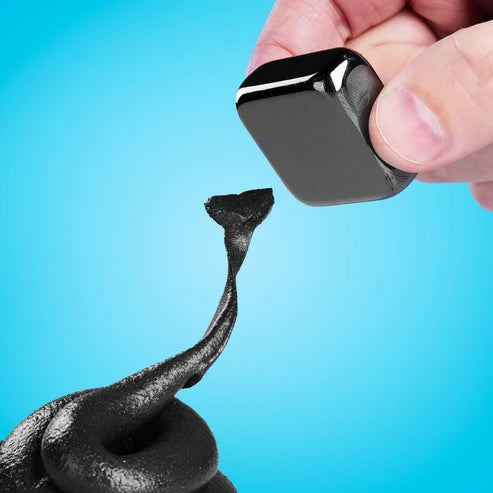Black magnetic cube attracting magnetic putty material against a blue background